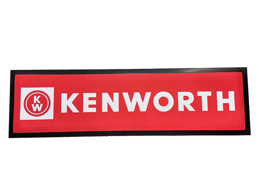 The BAR MAT RED KENWORTH features a rectangular red design with a black border, white Kenworth text, and a circular KW logo on the left—ideal for adding durable style to any home bar setup.