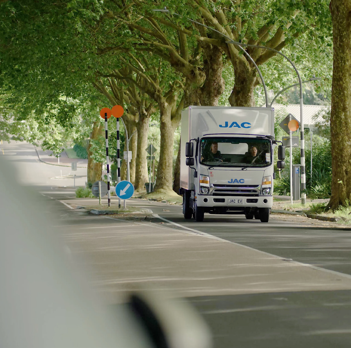 JAC electric truck driving along a tree-lined New Zealand street