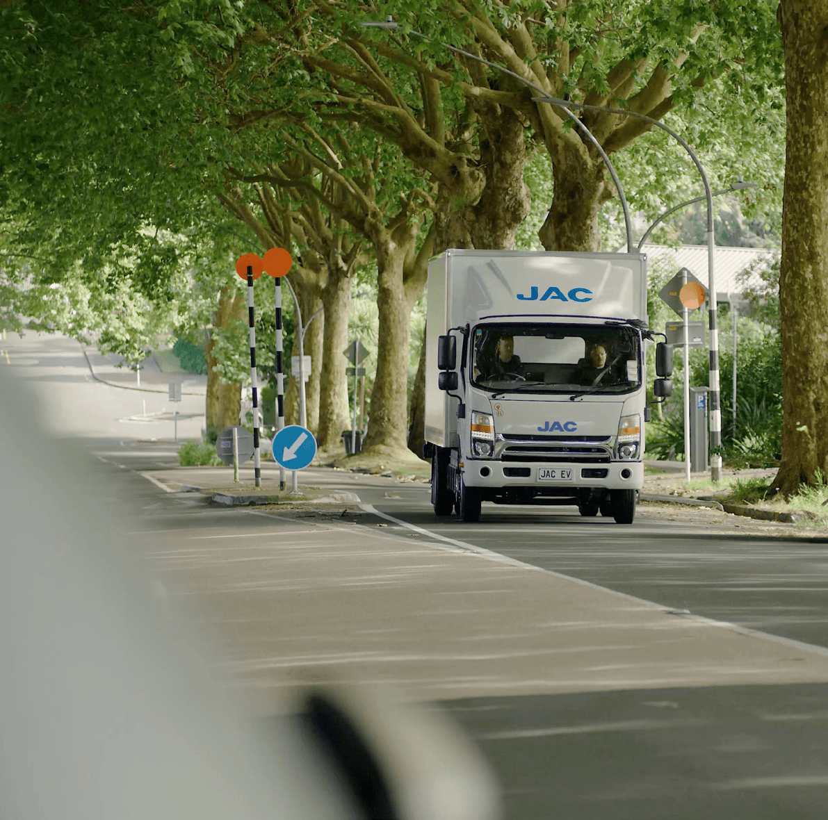 JAC electric truck driving along a tree-lined New Zealand street