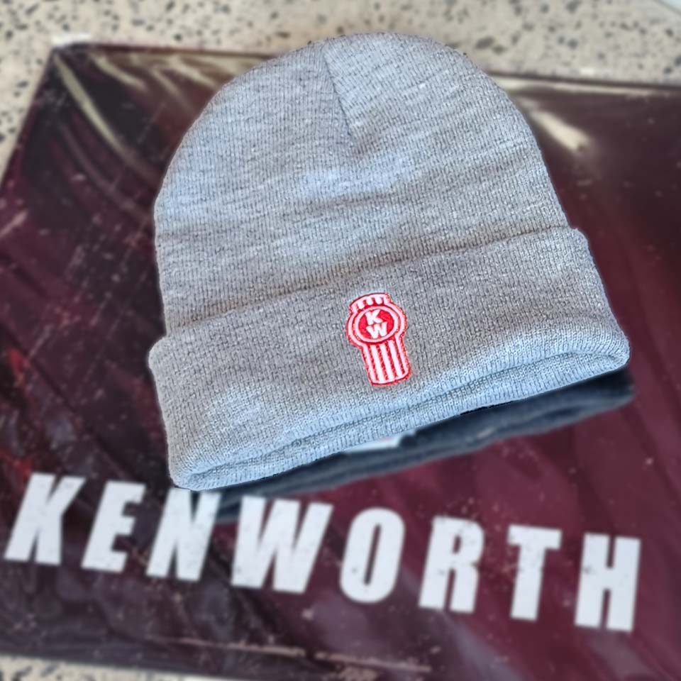 A BEANIE KW BLACK LED LIGHT, featuring a knit design and LED light, rests on a surface with a blurred Kenworth-branded background.