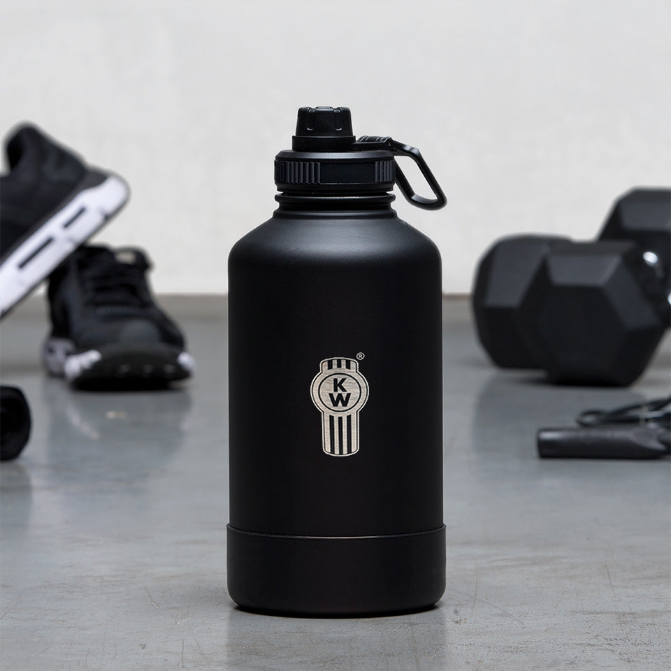 The BOTTLE KW ABSORPTION 1.9L, a durable black water bottle with a logo and flip-top lid, rests on a gym floor next to black athletic shoes, two dumbbells, and a jump rope.
