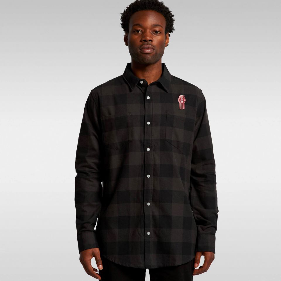 A man stands against a plain background wearing the SHIRT KW DRILL CHECK—a black and grey long sleeve checkered shirt featuring a small red and white embroidered logo on the left chest.