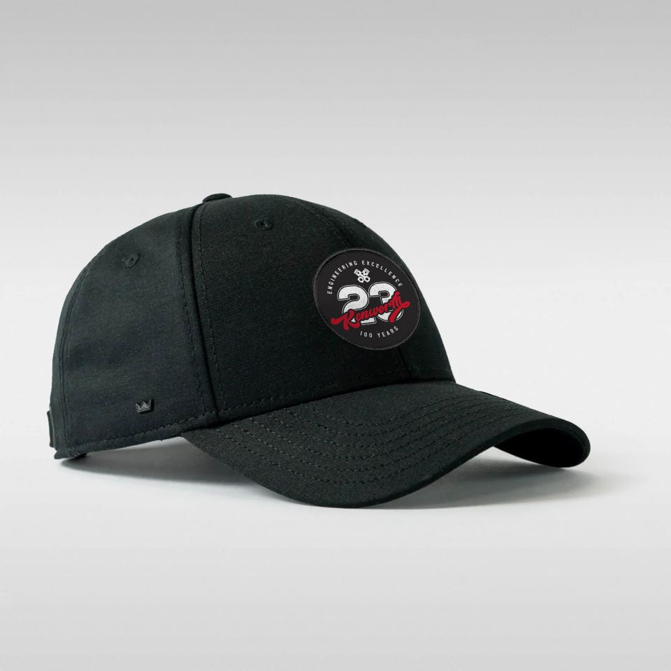 The CAP KW ENGINEERING EXCELLENCE is a black Kenworth cap with a round patch on the front displaying white text, a white car graphic, and red accents. It features UFlex fit for comfort and style, set against a plain light gray background.