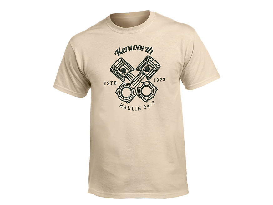 TEE SHIRT KW HAULIN SAND: Heritage-style sand tee with crossed engine pistons and bold black "Kenworth, ESTD. 1923" and "Haulin’ 24/7" text above and below the graphic.