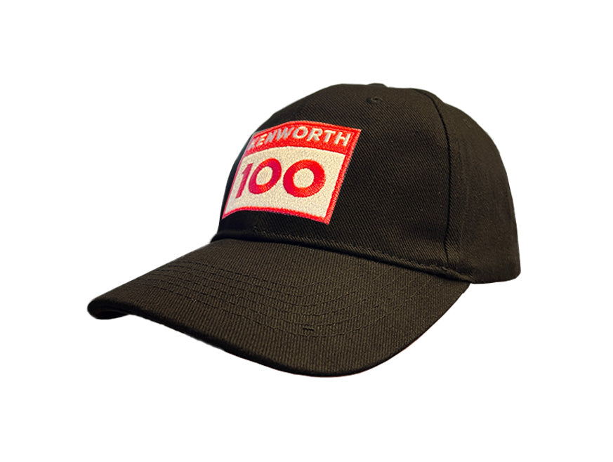 The CAP KW 100 YEARS BLACK is a limited edition black baseball cap with a bold red and white rectangular patch on the front, displaying KENWORTH 100 in striking letters and a sleek black finish.