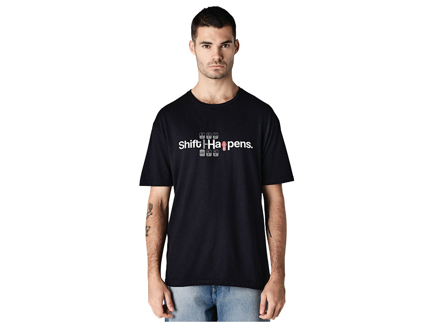 A man stands facing forward against a white background, wearing the TEE SHIRT KW SHIFT, a black Kenworth tee that features “Shift Happens” on the front with shift key icons cleverly replacing the “i” and “a.”.