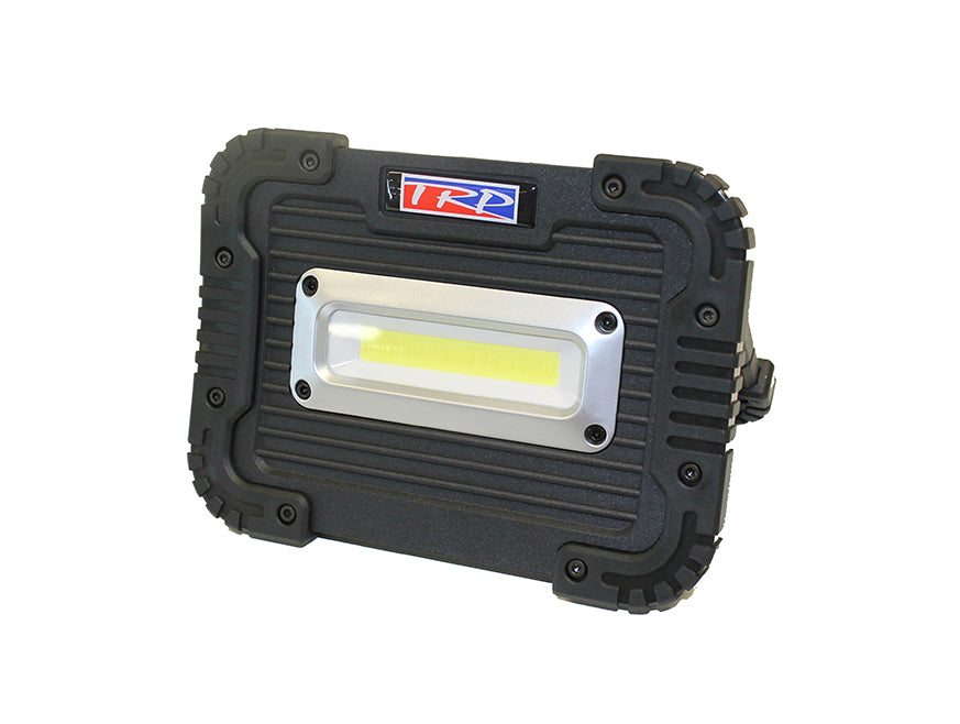 The TORCH LED TRP FREESTANDING is a portable black worklamp with a rugged rectangular build, ribbed edges for grip, a silver front panel with yellow LED strip, and a red, white, and blue TRP logo on top—ideal for roadside repairs.