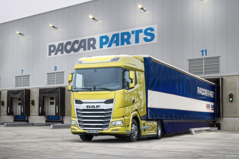 A yellow DAF truck with a blue and white PACCAR PARTS trailer is parked outside a building labeled PACCAR PARTS, near loading bays numbered 7, 8, and 11.