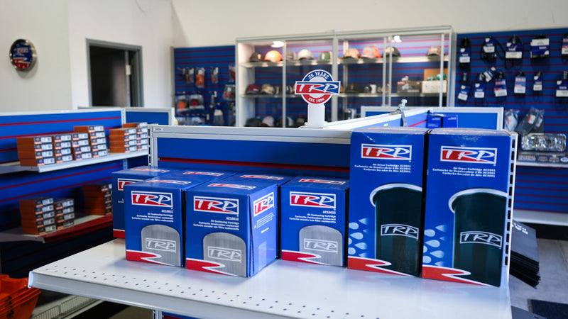 Shelves in a store displaying boxed TRP brand automotive parts, with more parts and accessories organized on wall shelves in the background.