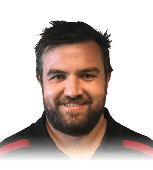A man with short dark hair and a beard, smiling, wearing a black shirt with red accents, in front of a white background.