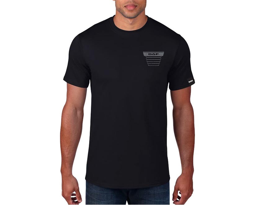 A man wears the TEE SHIRT DAF GRILLE—a plain black tee featuring a small gray D.A.R. logo and truck-inspired grille stripes on the left chest, plus a subtle sleeve tag—standing against a white background.