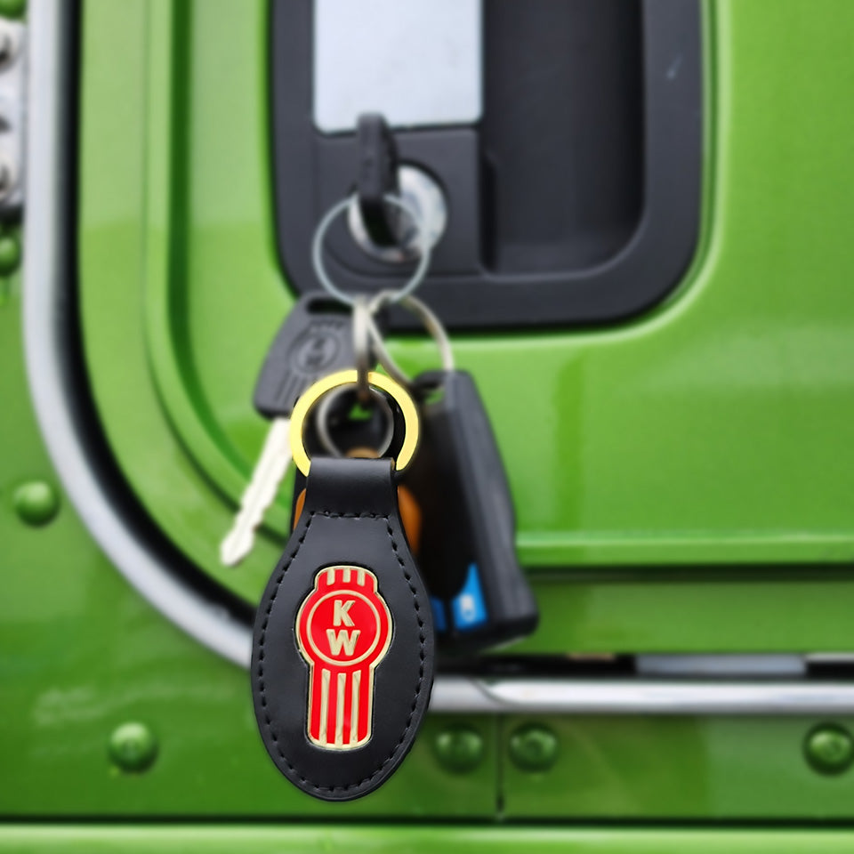 A close-up shows keys hanging from a green vehicle door lock. The KEYRING KENWORTH LEATHER, with its black leather and red-gold KW emblem, stands out in sharp focus, adding a touch of style to the scene.
