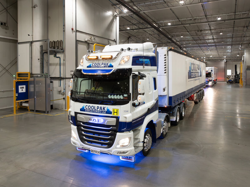 A large white and blue COOLPAK refrigerated truck with trailer parked inside a well-lit warehouse, ready for loading or unloading goods.