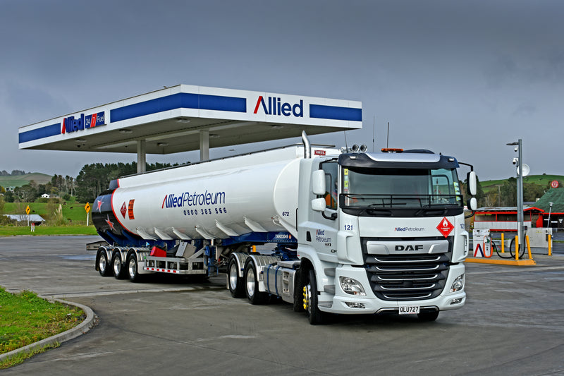 A white Allied Petroleum fuel tanker truck is parked at an Allied gas station under a large canopy, with trees and hills visible in the background.