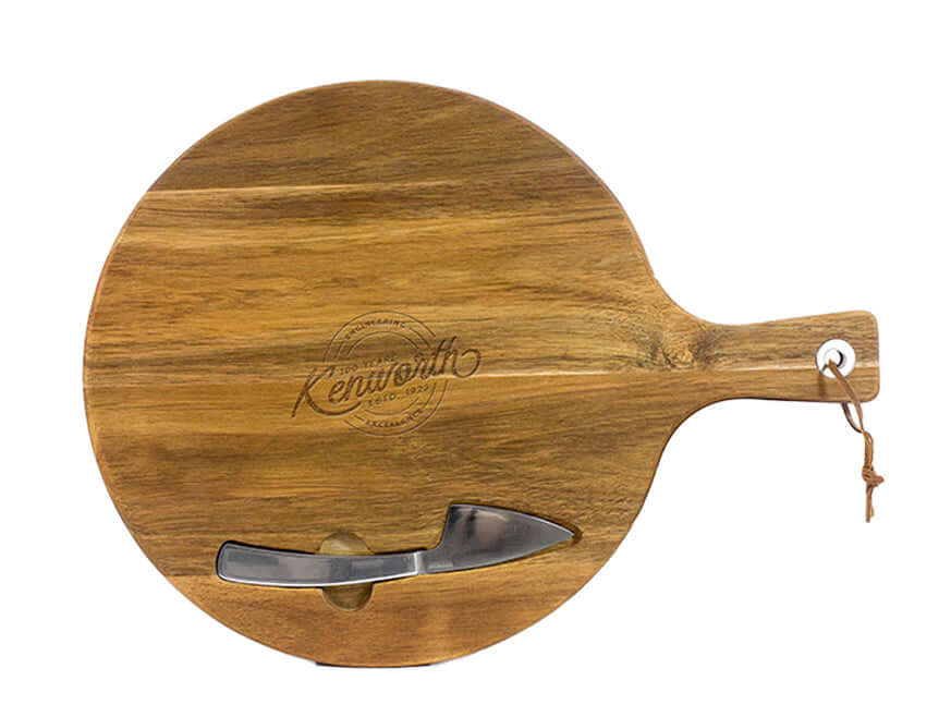 The WOOD BOARD AND KNIFE SET features a round natural wood cheese board with a handle, leather loop, and "Kenilworth" engraving. Includes a small metal-blade cheese knife that slots into a cutout at the base.