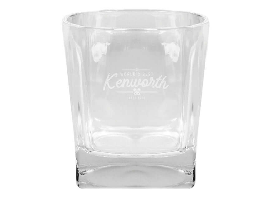 The TUMBLER KW GLASS is a clear glass tumbler with a square base, laser engraved on the front with "World's Best Kenworth Est. 1923." The empty glass is shown against a white background.