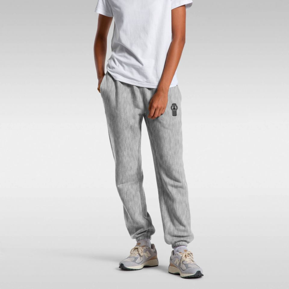 A person in a plain white t-shirt, SWEATPANT KW WOMENS GREY with a small black logo on the left thigh, and gray athletic shoes stands against a plain gray background.