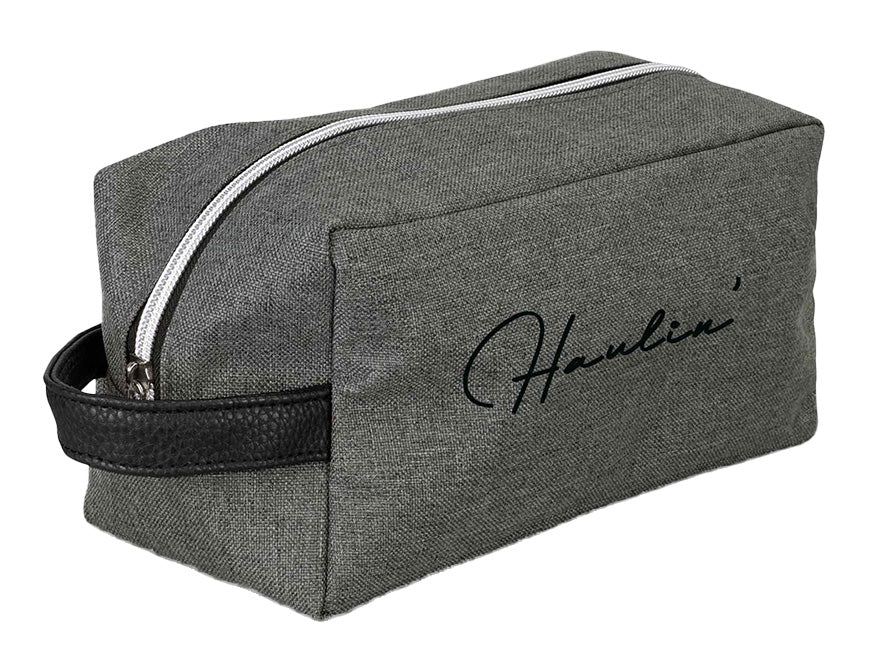 A rectangular gray BAG KW TOILETRY with a white zipper and black handle, ideal for travel. The word "Haulin’" is scripted on the side.