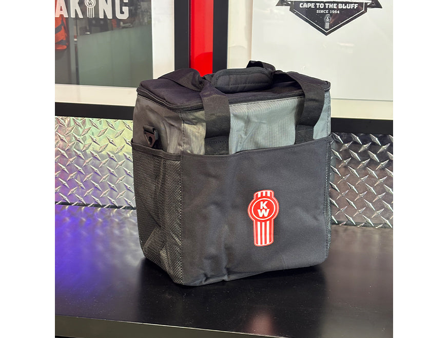 The BAG COOLER KW, a black and gray insulated lunch bag with short handles, features a circular red and white Kenworth logo on the front pocket. A convenient side mesh pocket adds to the cooler’s versatility, perfect for your needs.
