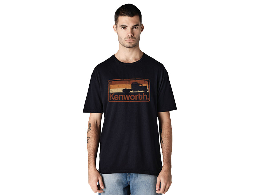 A man wearing a TEE SHIRT KW SHADOW, featuring a retro-inspired Kenworth truck shadow logo graphic, stands facing forward against a white background.