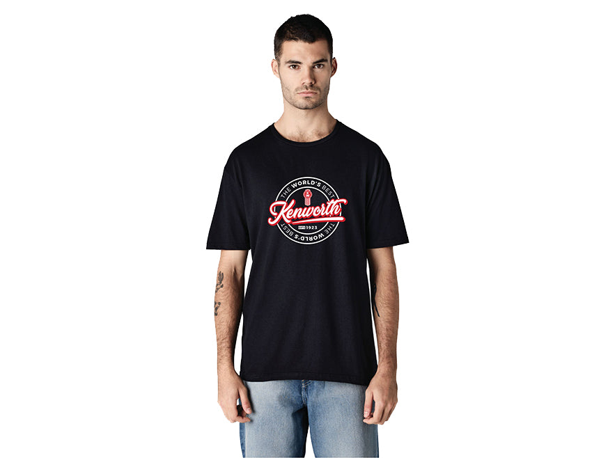 A man in light blue jeans faces forward with a neutral expression, wearing a black TEE SHIRT KW WORLDS featuring a red and white "The World’s Best" logo.