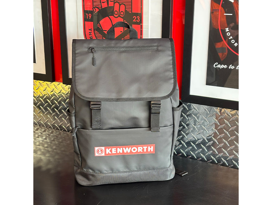 The BACKPACK KW ROLL TOP features a durable design with black straps and a red KENWORTH logo, displayed on a black surface against diamond plate metal and bold red-and-black artwork—ideal for daily use.