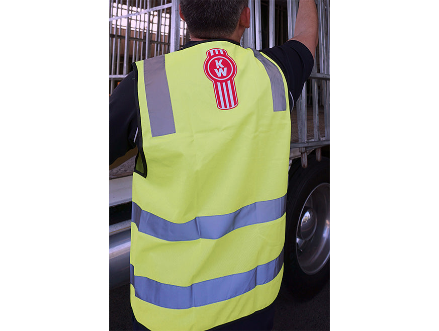 Wearing the VEST SAFETY KW BUG YELLOW, a person stands by a truck with their back to the camera—demonstrating how this high-visibility gear supports safety in work environments.