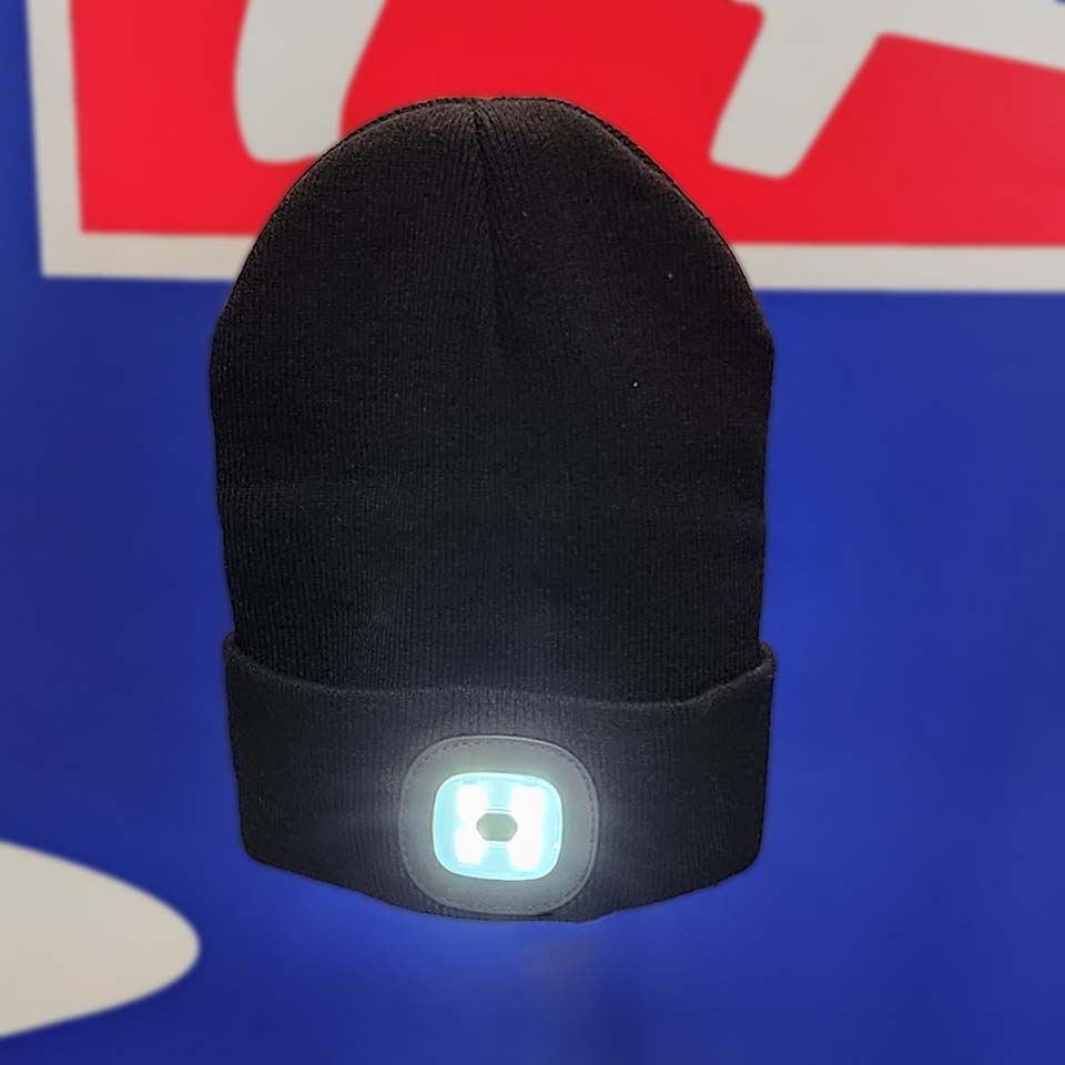 The BEANIE TRP BLACK LED is a black knit beanie with a bright front LED light, ideal for cold-weather activities, shown against a blue and red background with white shapes.