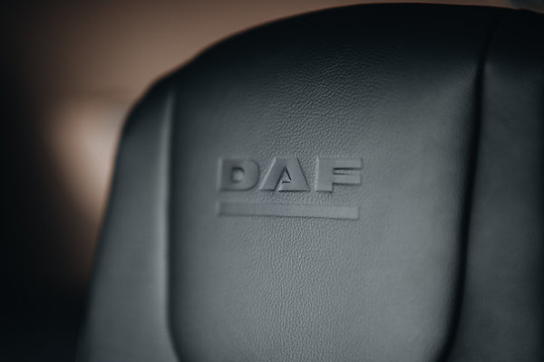 Close-up of a black leather seat with the embossed word DAF on the backrest, indicating the brand. The image focuses on the texture and logo detail.