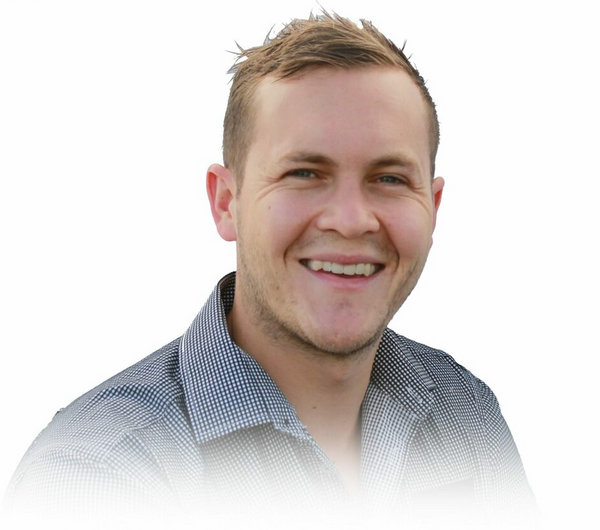 A smiling man with short, light brown hair is wearing a black and white checkered shirt. The background is white, and the lower part of the image fades out gradually.