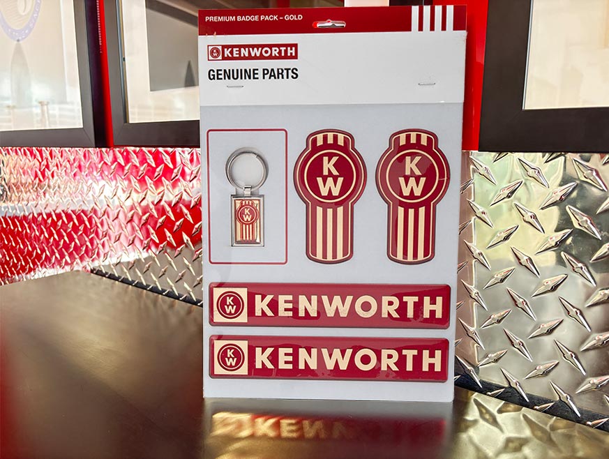 The DECAL KW SET GOLD PREMIUM includes two round red and gold emblems, a matching keychain, and two rectangular Kenworth badges, all displayed on a metallic diamond plate background.