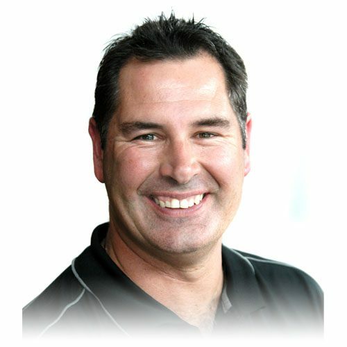Smiling man with short dark hair wearing a black collared shirt with white piping, pictured against a white background.