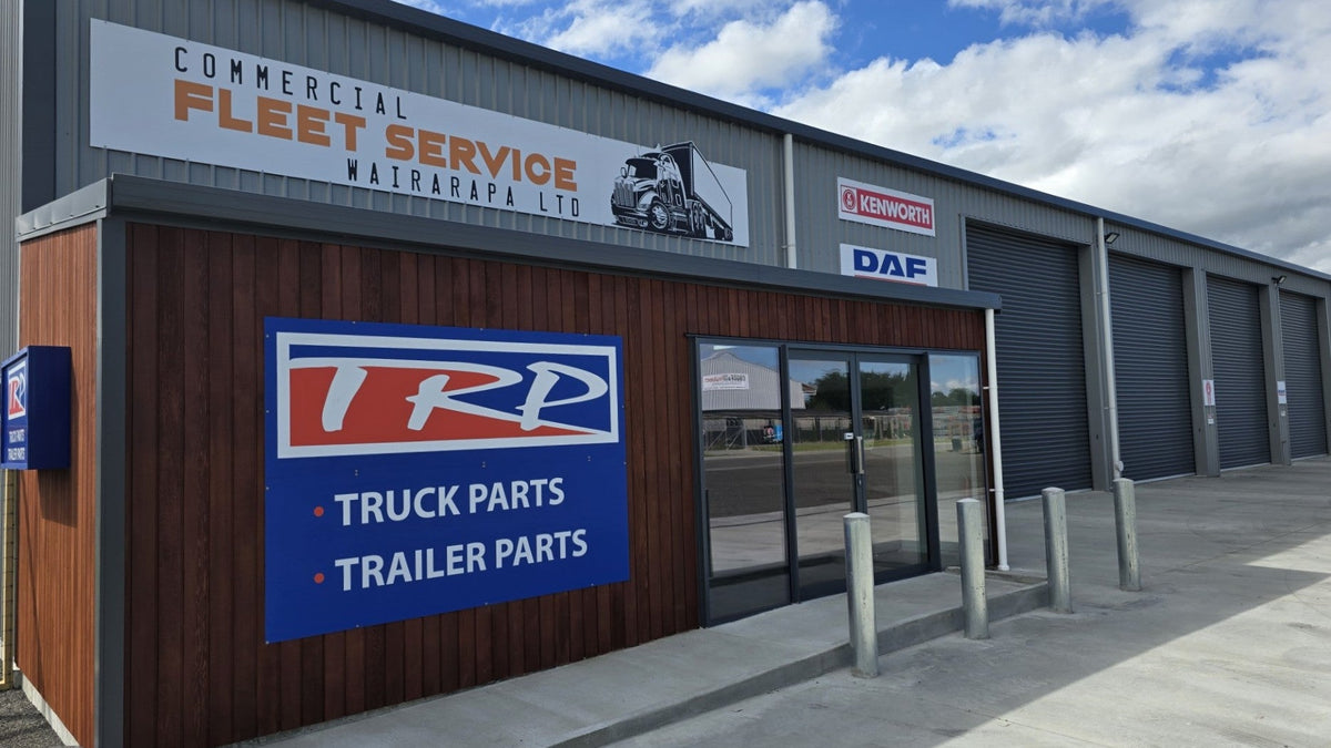 A commercial building with signs reading “Commercial Fleet Service Wairarapa Ltd” and “TRP Truck Parts Trailer Parts.” The building has large roller doors, a glass entrance, and a clear sky overhead.